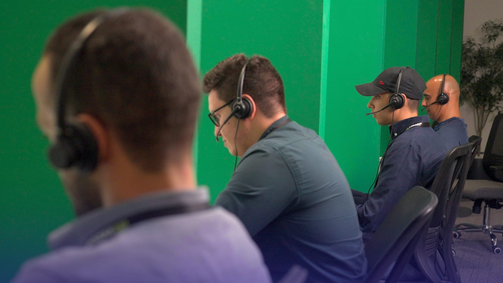 A row of call-center agents wearing headsets, seated side by side at their stations